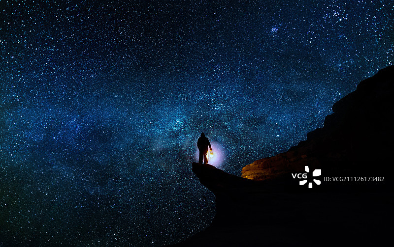 一個人站在懸崖上，身后是星空。圖片素材