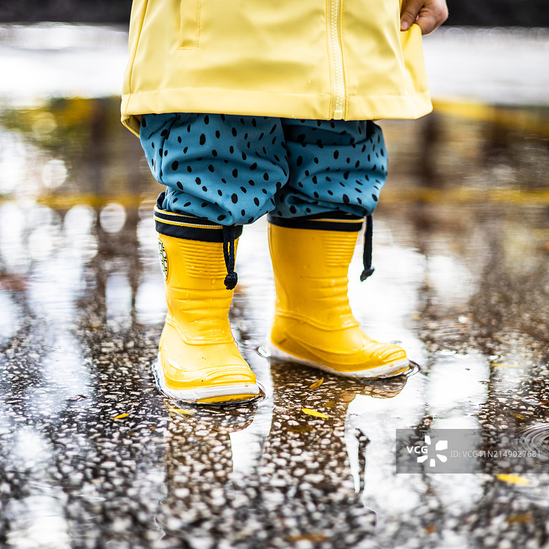 穿着黄色胶靴和防水雨衣的小男孩站在水坑里图片素材