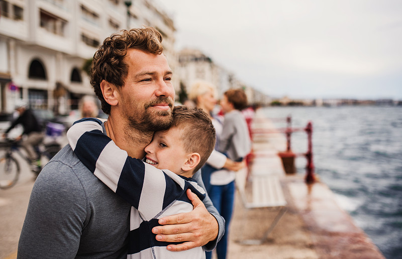 父親和小兒子站在海邊的小鎮上，擁抱著圖片素材