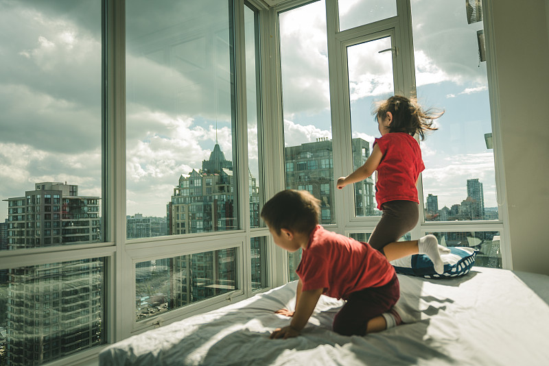 可愛的女孩和男孩在溫哥華的高層公寓的床上跳圖片素材