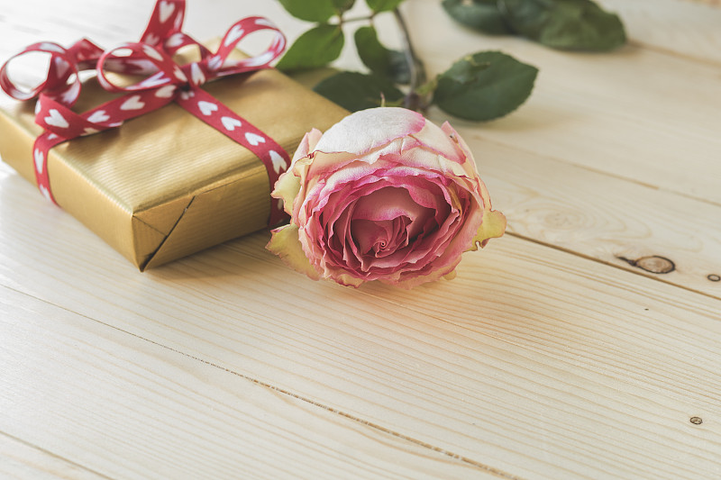 特寫的粉色玫瑰和禮品盒與心形絲帶在木制的背景。選擇性聚焦和復制空間圖片素材