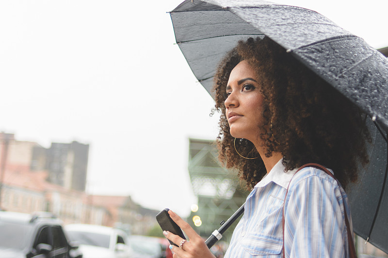 一名年輕女子在雨天用智能手機等出租車圖片素材