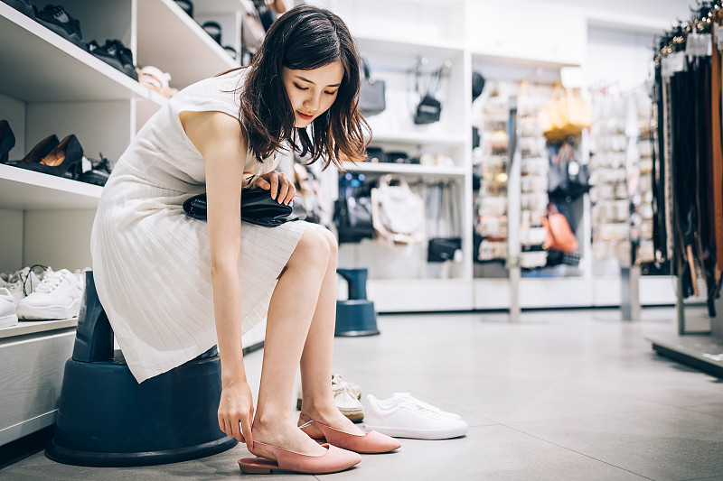 年輕的亞洲婦女在鞋店試穿一雙新涼鞋。圖片素材