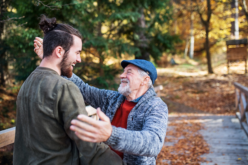 年老的父親和他的兒子在大自然中散步，擁抱和交談。圖片素材