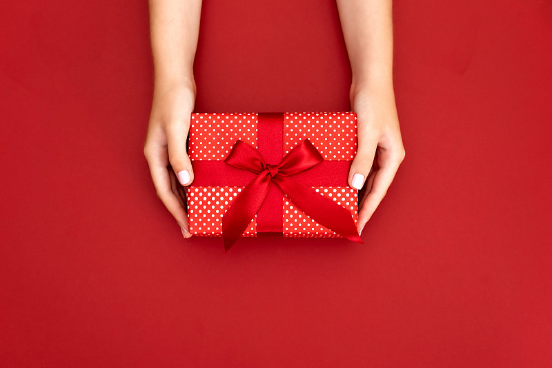 女性手握禮物與紅色的蝴蝶結在白色的鄉村閃閃發光的背景。節日背景:生日，情人節，圣誕節，新年。平躺圖片素材