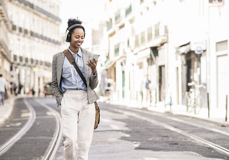 在葡萄牙的里斯本，一名年輕女子戴著耳機和手機，面帶微笑圖片素材