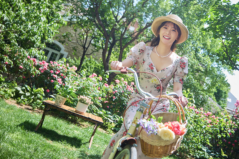 青年美女在开满鲜花的院子里骑自行车图片下载