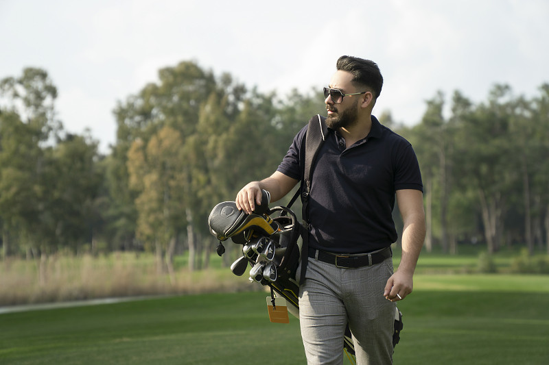 帥氣的年輕高爾夫球手的肖像攜帶著高爾夫球袋在高爾夫球場圖片素材