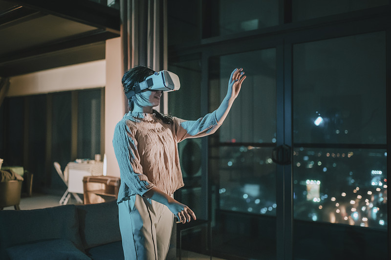 一位亞洲華裔少女戴上VR眼鏡，在客廳體驗3D虛擬游戲體驗圖片素材