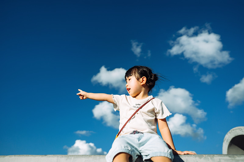 可愛的亞洲小女孩在戶外公園玩，指著美麗的藍天在一個可愛的陽光明媚的日子圖片素材