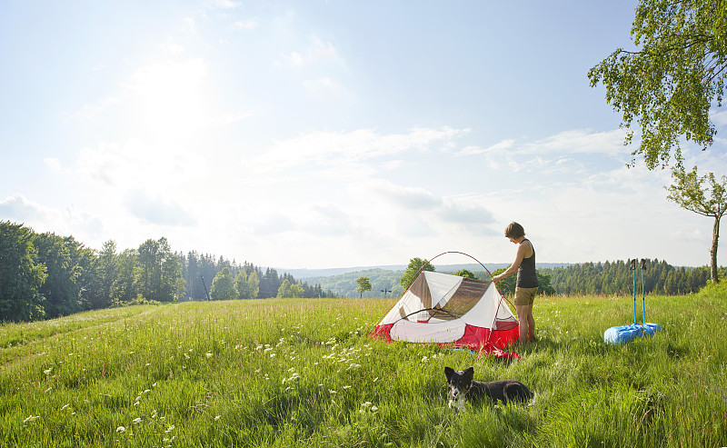 在陽光明媚的日子里，孤獨的女性在茂盛的草地上搭帳篷攝影圖片