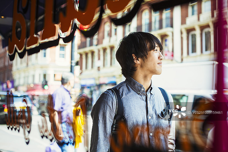一名年轻的日本男子在伦敦享受一天，走过一家商店的橱窗。图片素材