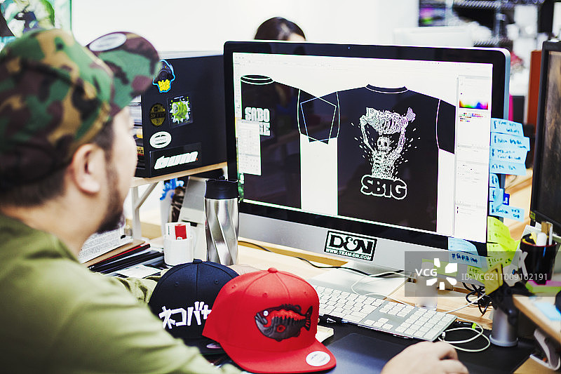 设计工作室。一名男子坐在桌前，用电脑设计t恤印花图案。图片素材