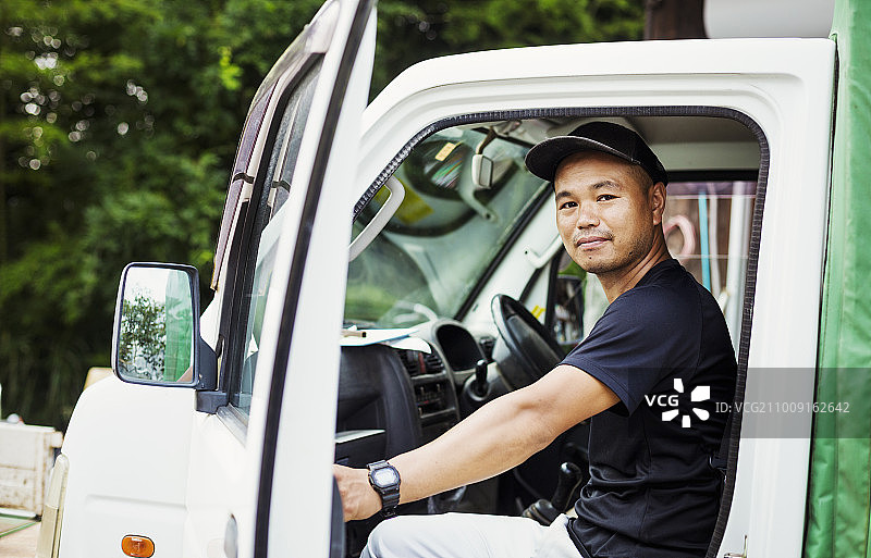 一个年轻人坐在卡车里，在日本的一个商业农场。图片素材