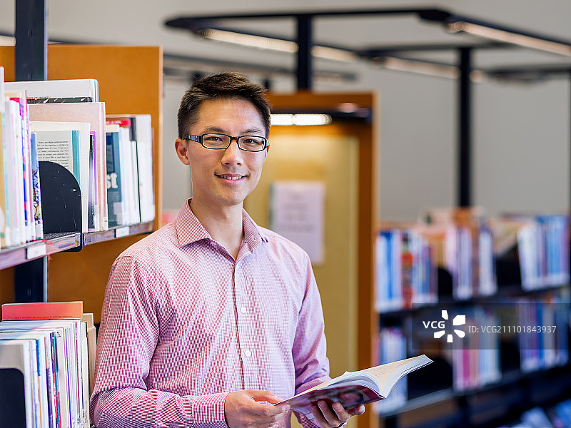 快乐的男学生拿着书在图书馆。快乐的亚洲男学生拿着书在图书馆图片素材