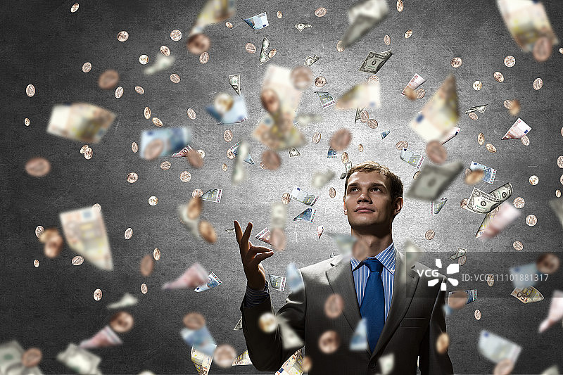 梦想着变得富有。年轻的商人站在钞票的雨中图片素材