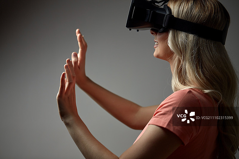 技术，增强现实，娱乐和人的概念-接近快乐的年轻女子与虚拟现实头盔或3d眼镜触摸看不见的东西图片素材