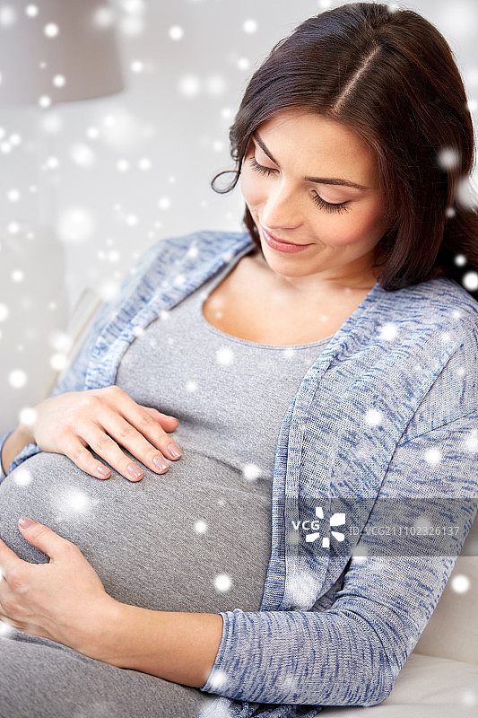怀孕，怀孕，冬天，人们和期望的概念-近距离的快乐孕妇与大肚子躺在家里的沙发上过雪图片素材