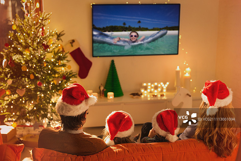 一家人戴着圣诞帽在圣诞客厅里看电视上的暑假视频图片素材