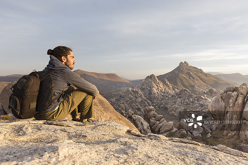 一个年轻人在岩石上放松，探索沙漠景观图片素材