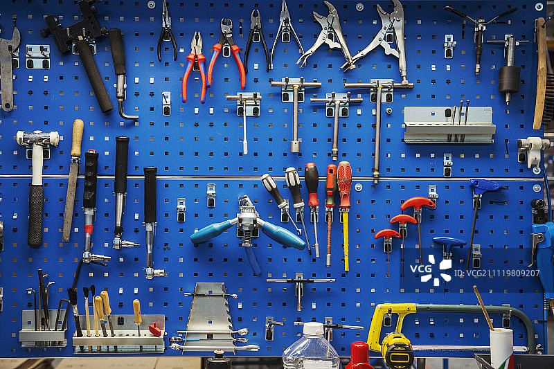 大量精选的手工工具整齐地挂在工厂或工作区墙上的蓝色工具板上。图片素材