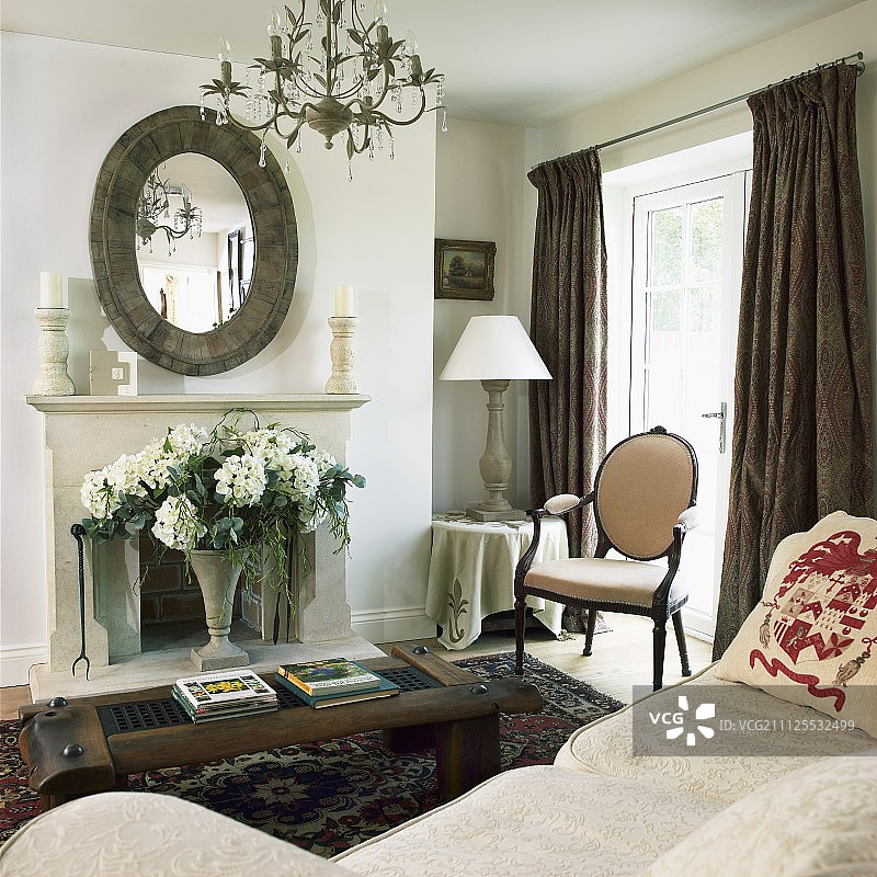 米色沙发前的质朴咖啡桌，壁炉上方的椭圆形镜子和古典客厅的古董椅子图片素材