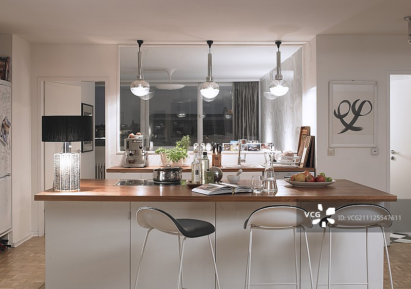 白色柜台和木制台面的吧台凳;一边有黑色灯罩的台灯，厨房柜台上方有球形灯罩的吊灯图片素材