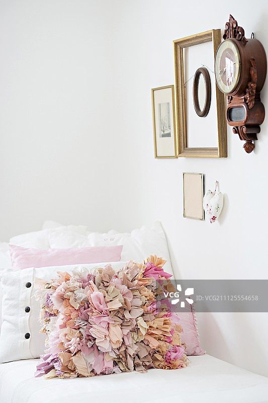 在沙发上的古董钟下面撒上粉色的褶皱坐垫，墙上挂着各种各样的相框图片素材