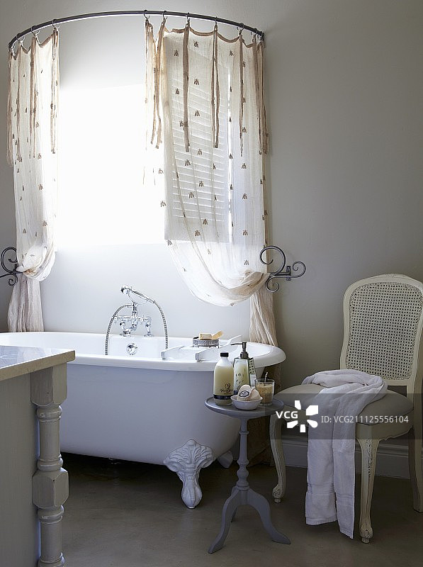 白色椅子和边桌，旁边是老式浴缸，浴帘下方是半圆形的帘轨图片素材