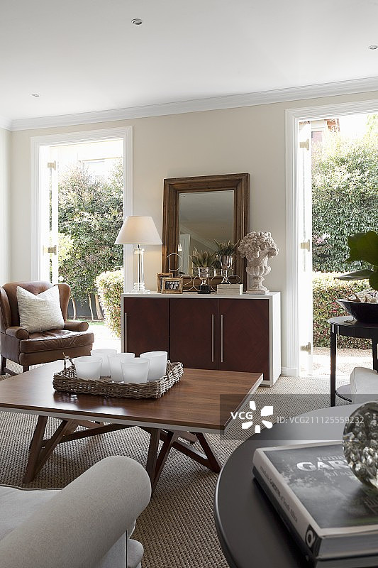 客厅有现代的木制咖啡桌，餐具柜两侧是开放式的露台门，可以看到种植的庭院图片素材