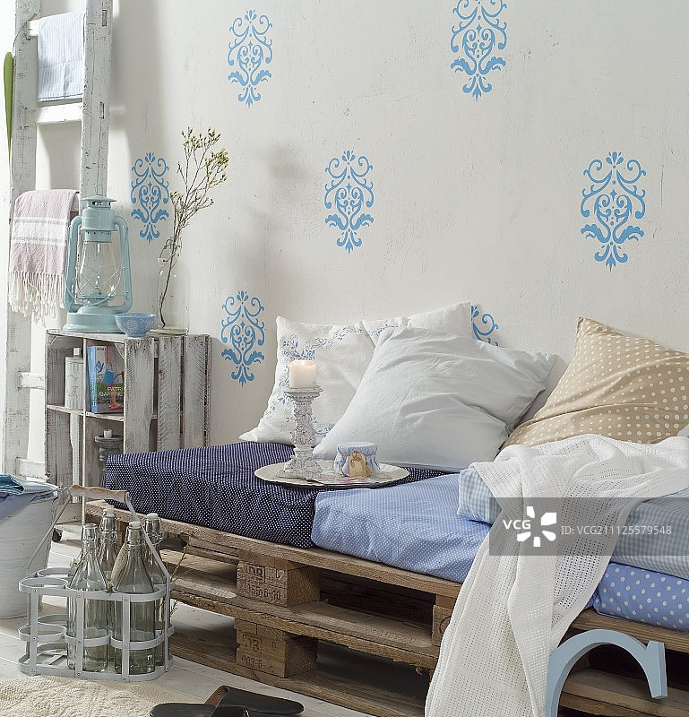 由木质托盘、坐垫和散垫改造而成的DIY沙发，以浅蓝色模板图案靠墙图片素材