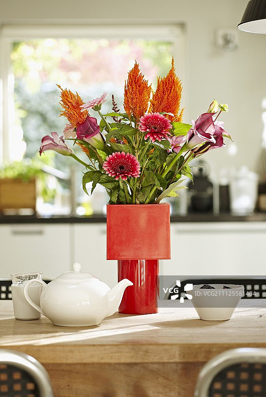 餐桌上的红色花瓶里，放着各种颜色的非洲菊和马蹄莲图片素材