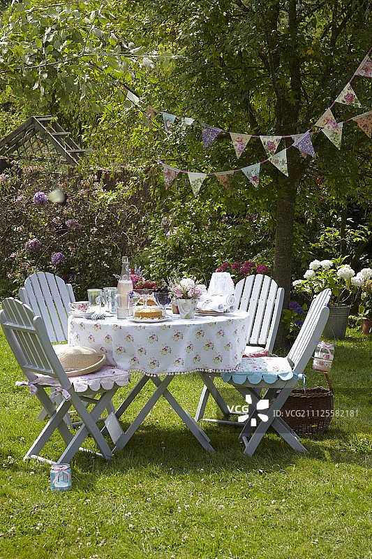 夏日花园派对，浪漫的餐桌，舒适的花园椅子与坐垫和复古风格的旗帜图片素材