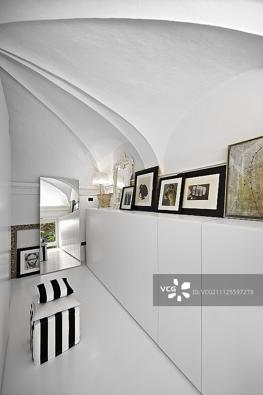 白色环氧树脂地板上有黑白条纹的Pouffe，旁边是白色的，拱形天花板下的现代餐具柜图片素材