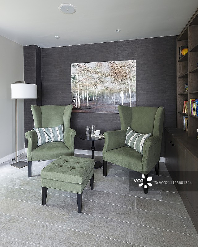 舒适的座椅区，书架旁的绿色扶手椅和脚凳图片素材