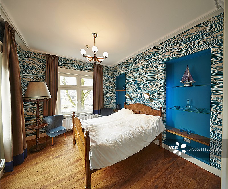 靠墙的木框双人床上贴着有图案的墙纸，书架上有蓝色的壁龛图片素材