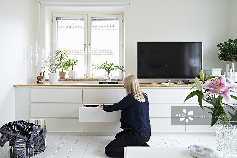 一个女人站在配有抽屉和平板电视的白色餐具柜前图片素材