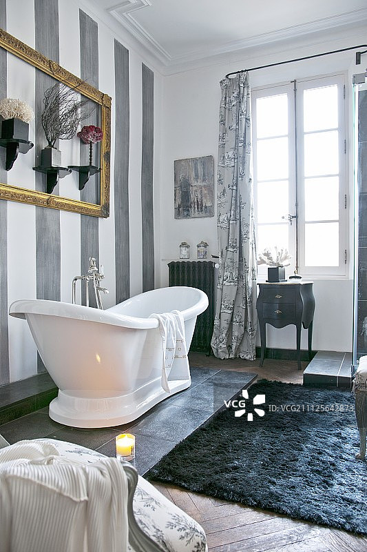 白色独立式浴缸，灰色条纹墙和格子落地窗在舒适的浴室图片素材