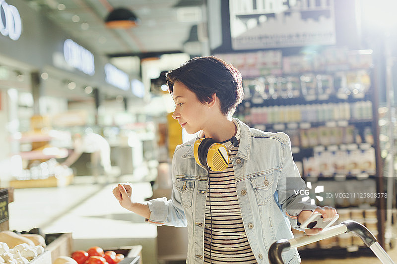 年轻女子戴着耳机浏览，在超市买菜图片素材