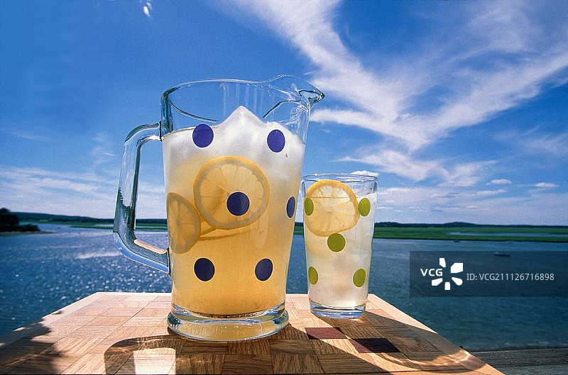一壶柠檬水和一杯柠檬水放在一张俯瞰湖面的桌子上图片素材