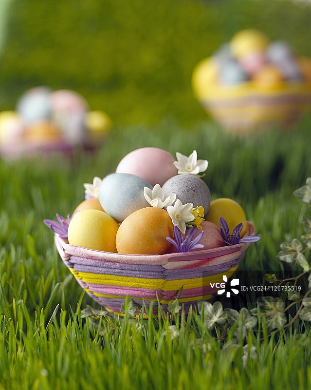 草地上的彩色复活节篮子，里面有鸡蛋和鲜花图片素材
