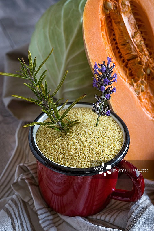 搪瓷杯子里放着蒸粗麦粉，背景是南瓜和白卷心菜图片素材