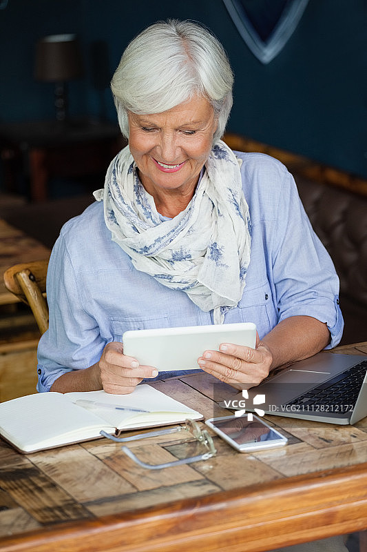 微笑的年长妇女使用数字平板电脑坐在桌旁的咖啡店图片素材
