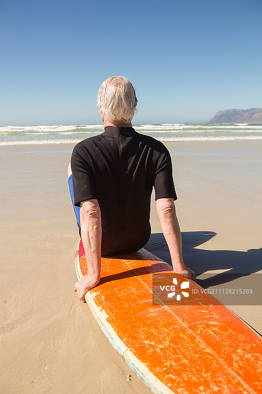 后视图的人坐在冲浪板上对着海边的海滩图片素材