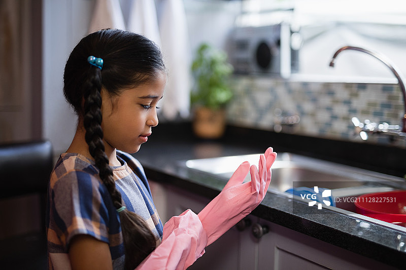 在厨房里戴着粉色橡胶手套的女孩的侧视图图片素材