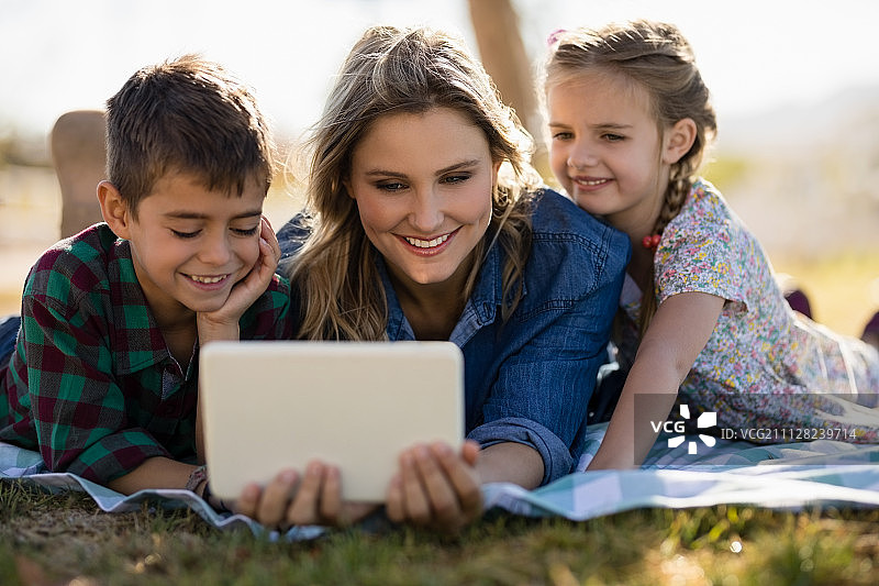 快乐的妈妈和孩子们在公园里使用数字平板电脑图片素材
