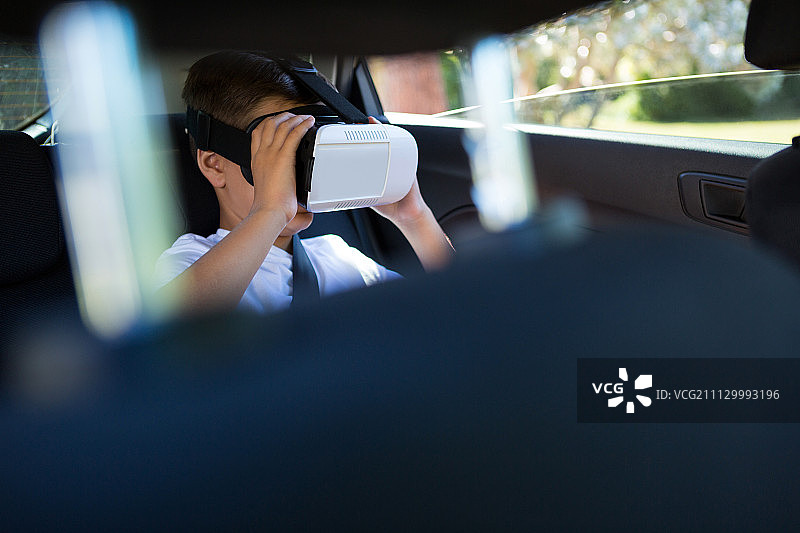 十几岁的男孩在汽车后座上使用虚拟现实耳机图片素材