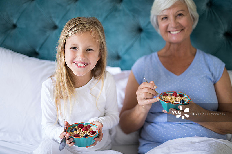微笑的孙女和祖母在床上吃早餐的肖像图片素材