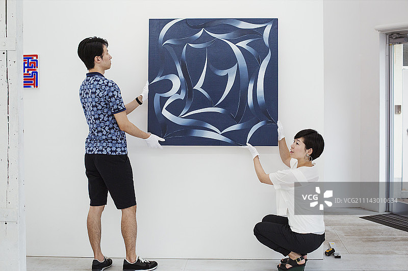 穿蓝衬衫的男人和穿白衬衫的女人在画廊的白墙上挂着现代绘画。图片素材