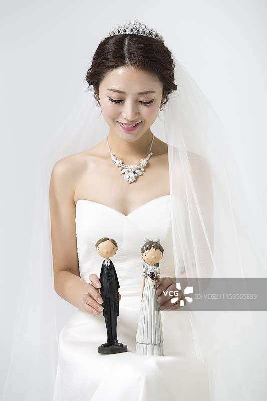 穿着婚纱的女人坐着抱着婚礼夫妇娃娃的摄影图片素材